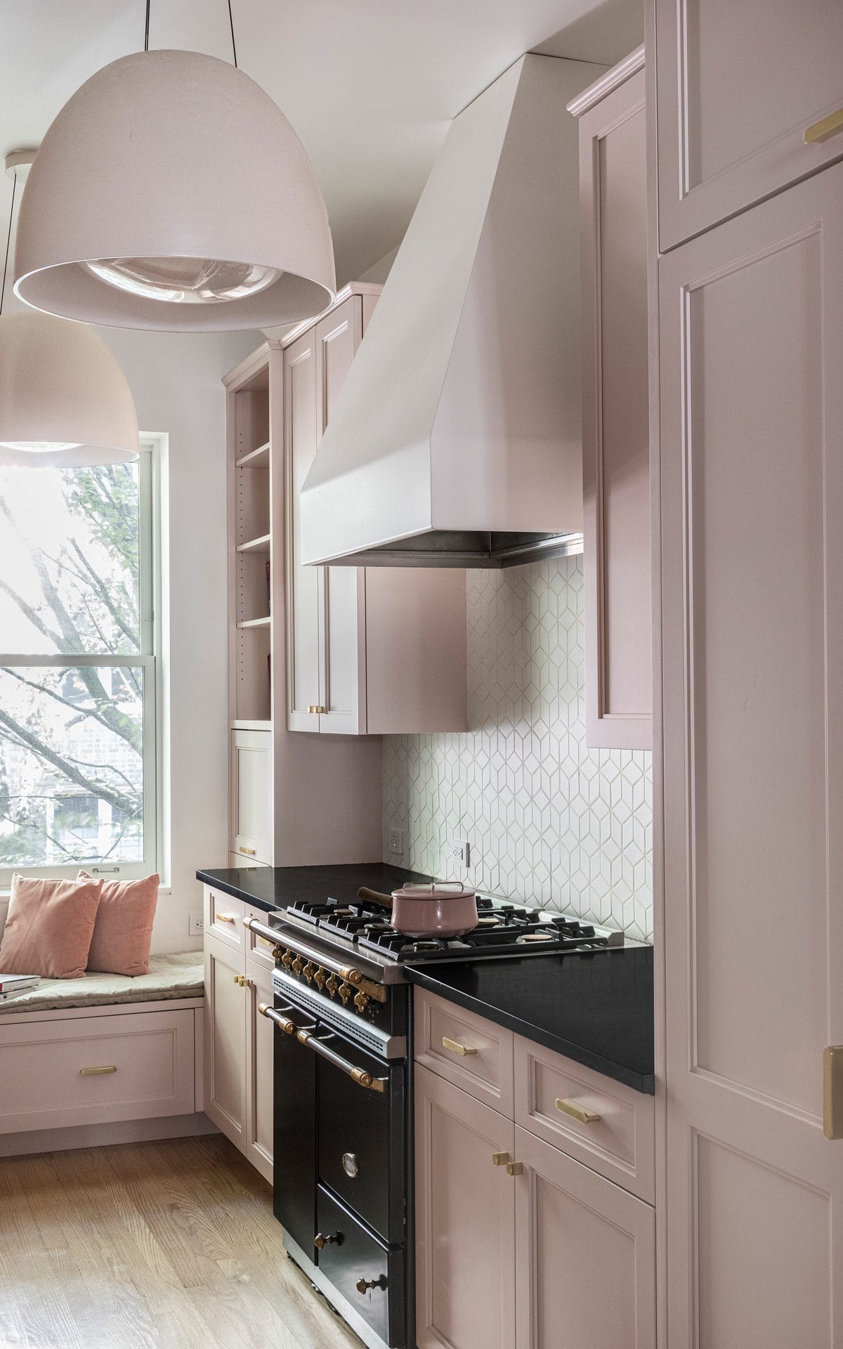 Modern dusty pink galley kitchen with black countertops and range